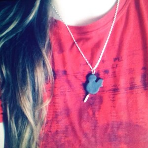 May include: A red t-shirt with a silver chain necklace featuring a black Mickey Mouse head pendant.