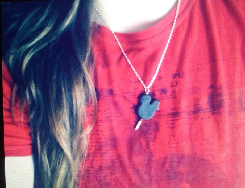 May include: A red t-shirt with a silver chain necklace featuring a black Mickey Mouse head pendant.