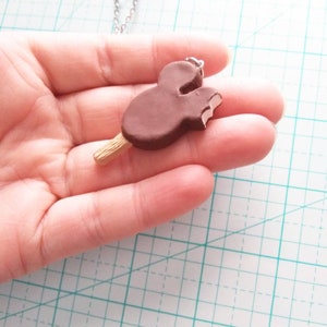 May include: A brown chocolate Mickey Mouse ice cream bar on a stick, with a bite taken out of it, is attached to a silver chain necklace.