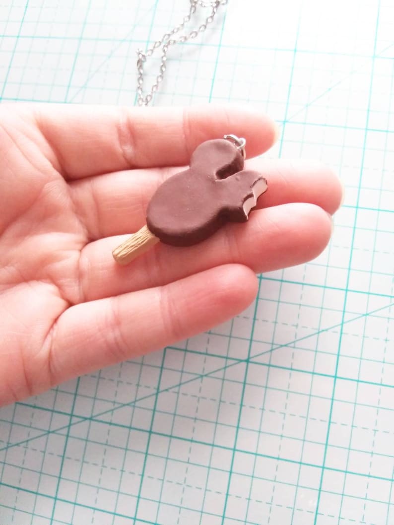 May include: A brown chocolate Mickey Mouse ice cream bar on a stick, with a bite taken out of it, is attached to a silver chain necklace.