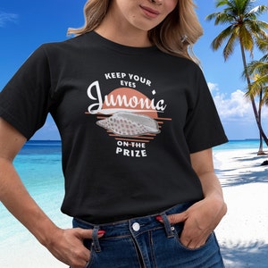 以下が含まれることがあります： 白い貝殻と「Keep your eyes on the prize Junonia」という文字が書かれた黒いTシャツ。