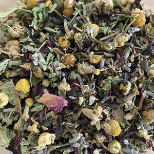May include: A close-up of a blend of dried herbs and flowers, including lavender, chamomile, and rose petals. The mixture is a light brown colour with hints of purple and pink.