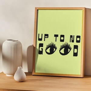May include: A framed print with a light green background and black text that reads "UP TO NO GOOD" with two black eyes in place of the "O"s.