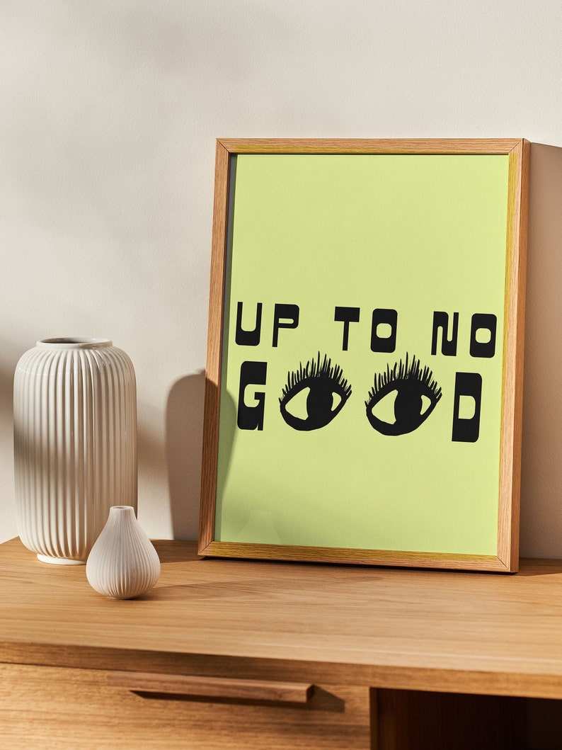 May include: A framed print with a light green background and black text that reads "UP TO NO GOOD" with two black eyes in place of the "O"s.