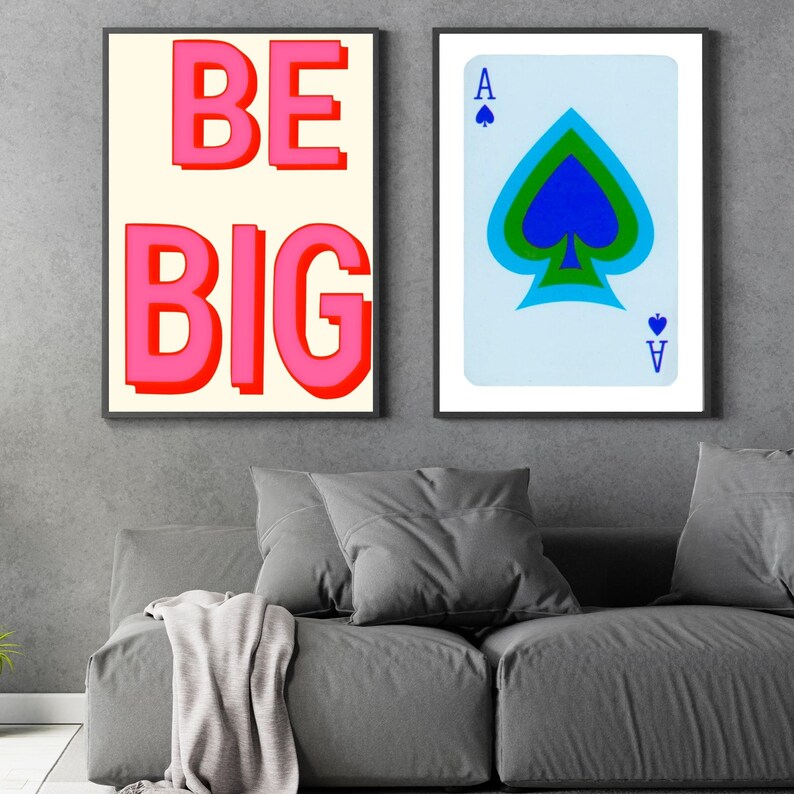 May include: Two framed prints, one with the text "BE BIG" in pink letters on a white background, and the other with a blue and green ace of spades playing card on a light blue background.