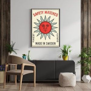 May include: A framed vintage-style poster with the text "SAFETY MATCHES" above a red sun design with blue rays. The poster also includes the text "FINEST QUALITY" and "MADE IN SWEDEN".