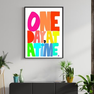 May include: A colorful typography print with the text "ONE DAY AT A TIME." The letters are in different colors, including pink, orange, red, yellow, green, blue, and purple.