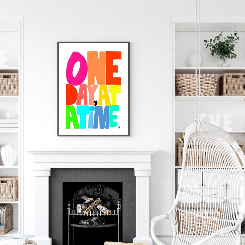 May include: A colorful typography print with the text "ONE DAY AT A TIME." The print is framed in black and is hanging on a white wall above a fireplace.
