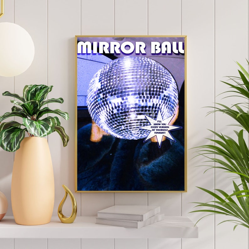 May include: A poster with the text "MIRROR BALL" in white letters on a blue background. A large silver disco ball is in the center of the poster, partially obscured by a person's hand. The text "I'LL SHOW YOU EVERY VERSION OF YOURSELF TONIGHT!" is in a white starburst shape.