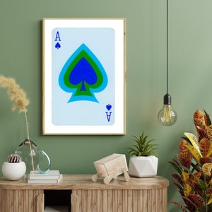 May include: A framed print of an Ace of Spades playing card with a blue, green, and black spade design. The card has a white background and blue lettering.