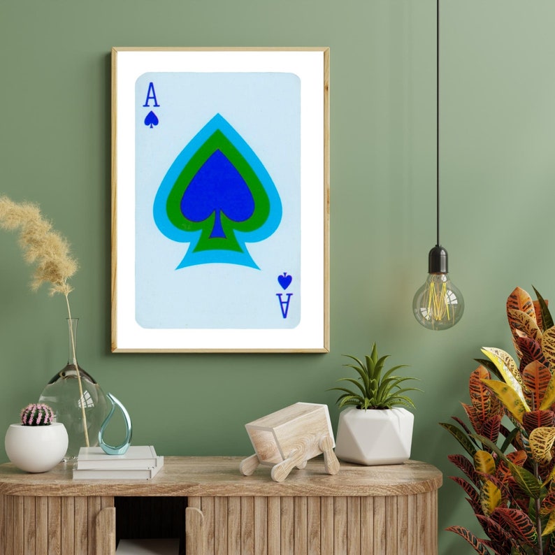 May include: A framed print of an Ace of Spades playing card with a blue, green, and black spade design. The card has a white background and blue lettering.