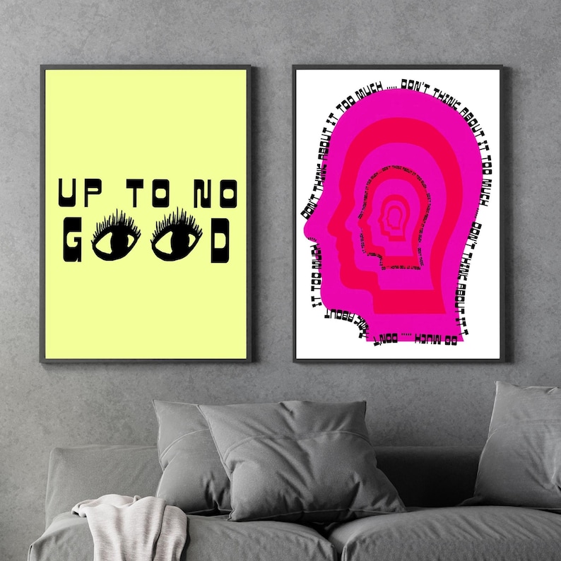 May include: Two framed prints with black frames. The print on the left has a yellow background with black text that reads "UP TO NO GOOD" and two black eyes. The print on the right has a white background with a pink silhouette of a head with the text "DON'T THINK ABOUT IT TOO MUCH... DON'T THINK ABOUT IT TOO MUCH... DON'T THINK ABOUT IT TOO MUCH... DON'T THINK ABOUT IT TOO MUCH..."