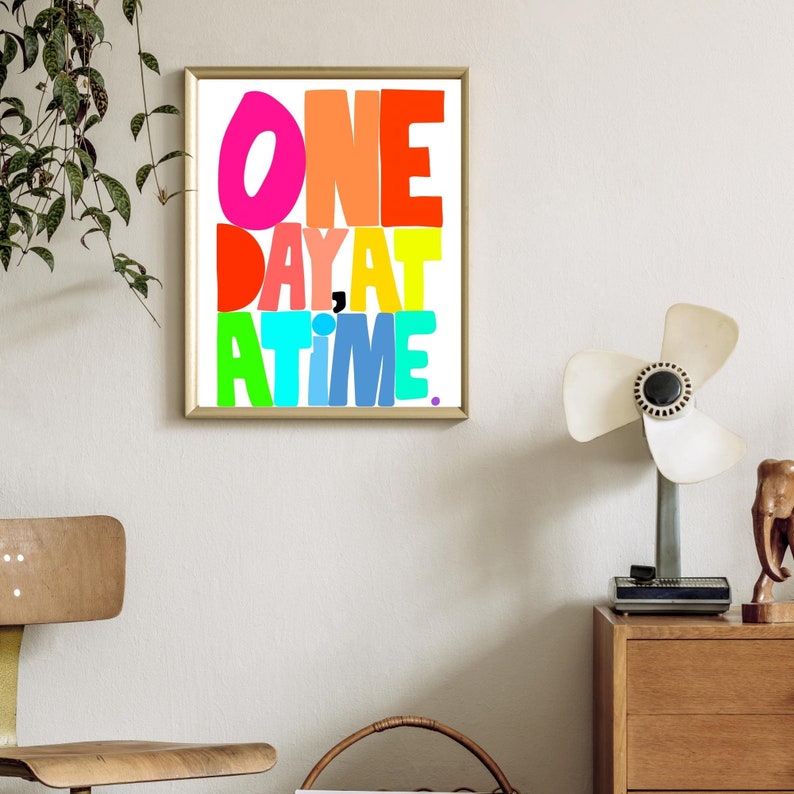May include: A framed print with the text "ONE DAY AT A TIME" in colorful, overlapping letters. The letters are in shades of pink, orange, yellow, green, blue, and turquoise.