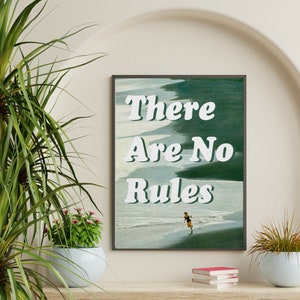 May include: A framed print with a green and blue watercolor background. The text "There Are No Rules" is written in white, bold letters. A person in a swimsuit is walking on a beach in the background.