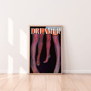 Op de afbeelding: Een poster met het woord "DREAMER" in grote witte letters op een zwarte achtergrond. Twee paar benen zijn afgebeeld met glinsterende, rode kousen.