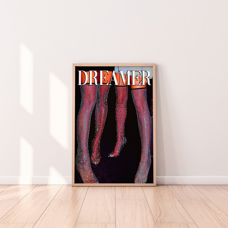 Op de afbeelding: Een poster met het woord "DREAMER" in grote witte letters op een zwarte achtergrond. Twee paar benen zijn afgebeeld met glinsterende, rode kousen.