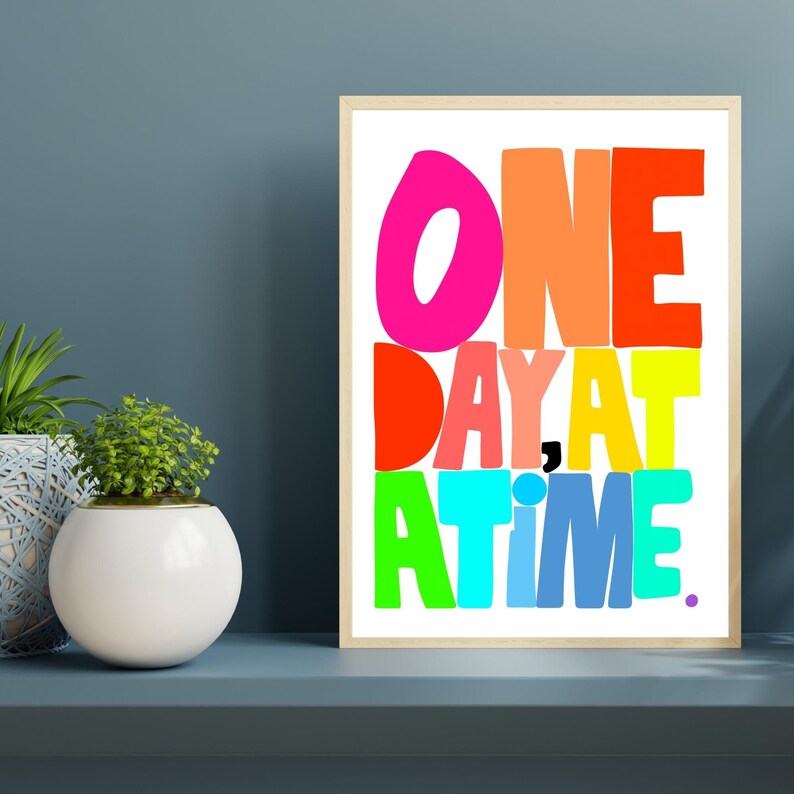 May include: A colorful framed print with the text "ONE DAY AT A TIME." The letters are in different colors, including pink, orange, red, yellow, green, blue, and purple.