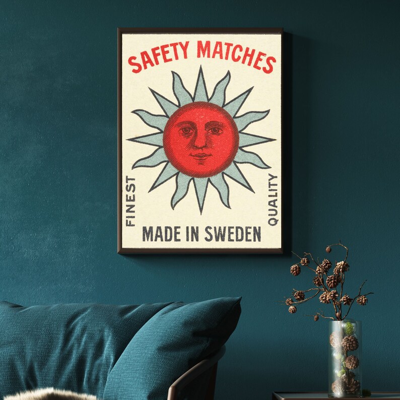 May include: Framed vintage poster featuring a red sun with a face, surrounded by light blue rays. The text "SAFETY MATCHES" is at the top, with "FINEST QUALITY" on the sides, and "MADE IN SWEDEN" at the bottom. The poster is in a black frame.