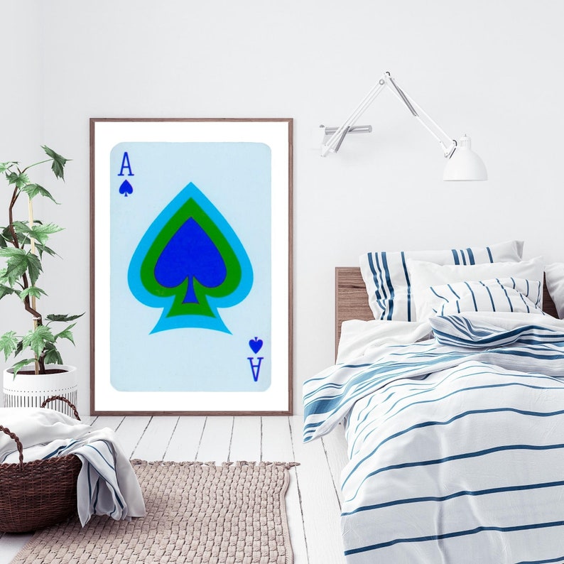 May include: A framed print of the Ace of Spades playing card. The card is blue, green, and white with a black spade symbol. The card is framed in a brown frame and is hanging on a white wall.