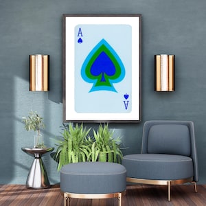 May include: A framed print of an ace of spades playing card with a blue, green, and black spade design. The card is on a light blue background. The print is hanging on a blue wall with two gold wall sconces on either side.