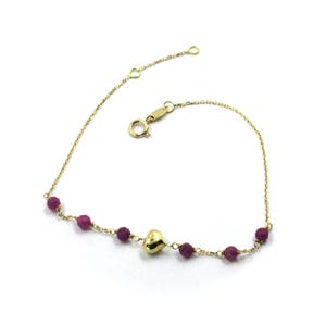 May include: A gold chain bracelet with a small heart charm and purple beads.