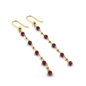 Peut inclure: Boucles d'oreilles en or avec une chaîne de petites perles rouges.