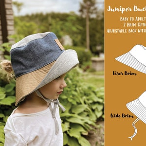 May include: A gray and blue bucket hat with a brown brim. The hat has an adjustable back with a pony hole. The hat is available in two brim styles: visor and wide.  Juniper Bucket Hat. Baby to Adult Size. 2 Brim Options. Adjustable Back with Pony Hole.