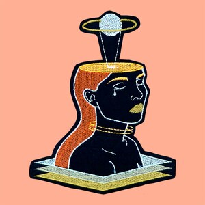 May include: Embroidered patch depicting a person with an open head, a planet above, and a layered base. The design uses black, orange, gold, and white thread on a peach background. The person has a tear and gold lips.