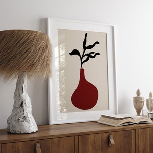 Może przedstawiać: Biały obraz w ramie z beżowym tłem przedstawiający czarną sylwetkę rośliny w czerwonym wazonie.