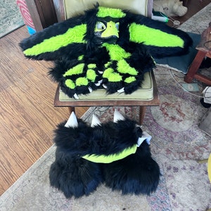May include: A black and neon green furry costume set, including a headpiece, body suit, and foot paws. The headpiece has a yellow beak and eyes. The body suit and foot paws feature white claws. The costume is designed with a combination of black and neon green fur.