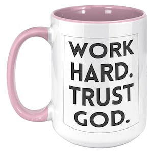 May include: White ceramic mug with a pink interior and handle. The mug features the text "WORK HARD. TRUST GOD." in a black, bold font, centered on the front. The mug is designed for hot beverages.