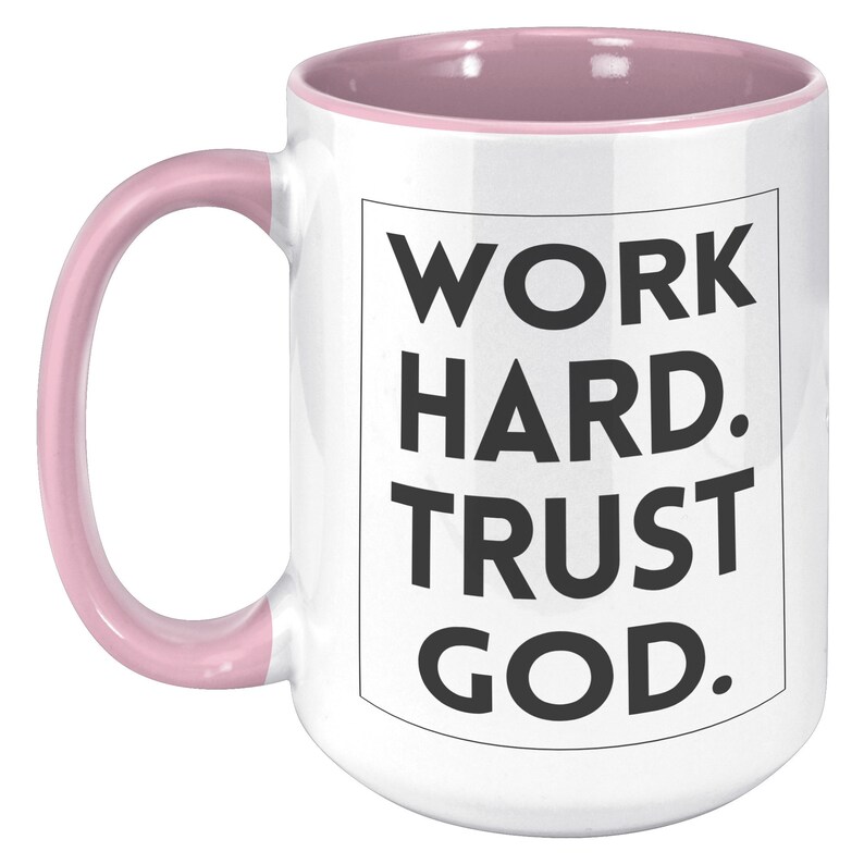 May include: White ceramic mug with a pink interior and handle. The mug features the text "WORK HARD. TRUST GOD." in a black, bold font, centered on the front. The mug is designed for hot beverages.