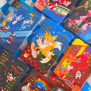 May include: Rectangular, glossy Sonic the Hedgehog character designs. Each features a different character, the words "SCORE TIME RINGS", and the number "9999". The backgrounds are various colors, including blue, red, and yellow.