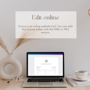 May include: A laptop computer displaying a Canva invoice template on the screen. The laptop is on a wooden table with a vase of dried pampas grass, a pair of glasses, and a stack of white paper. A cup of coffee is on the stack of paper. The text on the screen reads "INVOICE".