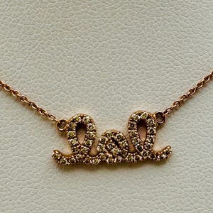 May include: Rose gold necklace with the word "Soul" spelled out in a cursive font. The letters are encrusted with small, sparkling stones. The necklace is displayed on a white surface.
