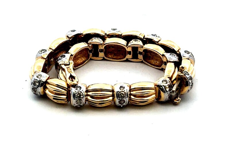 May include: A gold and silver bracelet with a chain link design and small clear stones. The bracelet has a clasp closure.