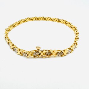 May include: A gold tennis bracelet with a diamond-encrusted design. The bracelet features a delicate chain with small diamonds set in a criss-cross pattern.