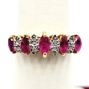 Puede incluir: Un anillo de banda de oro con una fila de piedras de rubí y diamante de forma marquesa. Las piedras de rubí son de color rosa intenso y los diamantes son transparentes.