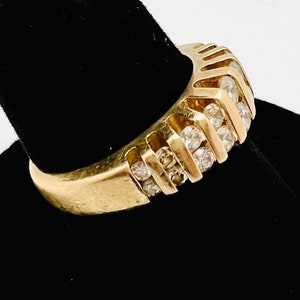 May include: A gold band ring with a row of small, clear diamonds set in a chevron pattern.