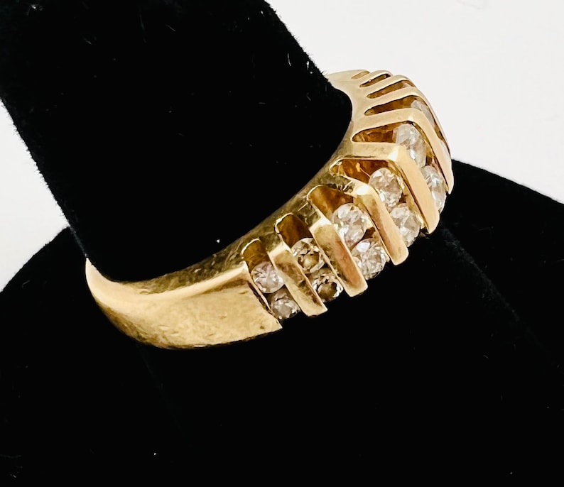 May include: A gold band ring with a row of small, clear diamonds set in a chevron pattern.