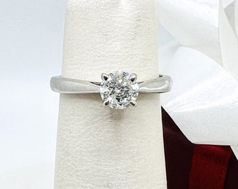 Puede incluir: Un anillo de compromiso de plata con un diamante redondo y transparente engastado en garras.