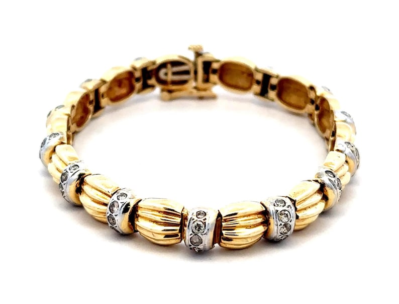 May include: A gold bracelet with a braided design and small clear stones set in the metal. The bracelet has a clasp closure.