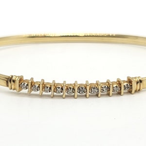 May include: A gold bangle bracelet with a row of small diamonds set in square-shaped settings.