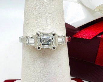 May include: A platinum engagement ring with a center emerald cut diamond and two baguette diamonds on the sides.