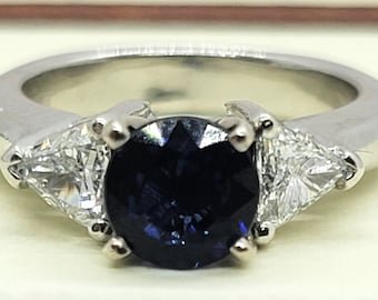 May include: A silver ring with a large, dark blue gemstone surrounded by two smaller, triangular, clear gemstones.