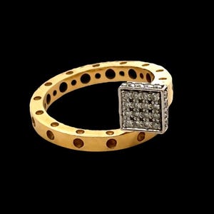 Könnte beinhalten: Ein goldfarbener Ring mit einem quadratischen, diamantbesetzten Mittelstück. Das Ringband weist gleichmäßig verteilte kreisförmige Aussparungen auf. Das quadratische Mittelstück ist silberfarben und mit kleinen, klaren Diamanten besetzt. Der Ring ist vor schwarzem Hintergrund.