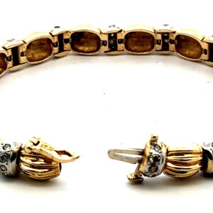 May include: A gold and white bracelet with a diamond-encrusted design. The bracelet is made of linked oval-shaped pieces with a braided pattern.