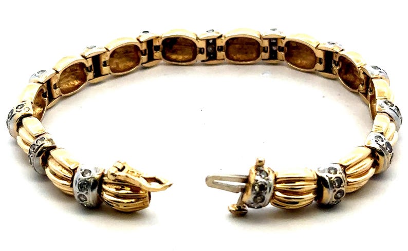 May include: A gold and white bracelet with a diamond-encrusted design. The bracelet is made of linked oval-shaped pieces with a braided pattern.