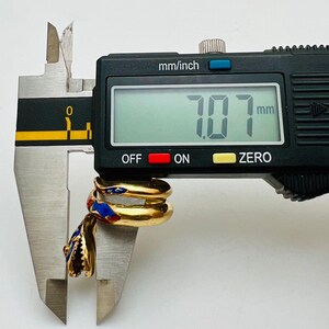 May include: A gold-toned ring with a snake design, featuring red and blue enamel details. The ring is measured with a digital caliper, displaying a measurement of 7.07 mm.
