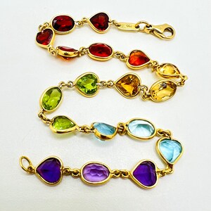 May include: A gold bracelet with a rainbow of heart-shaped and oval gemstones. The bracelet features red, orange, yellow, green, blue, and purple stones.